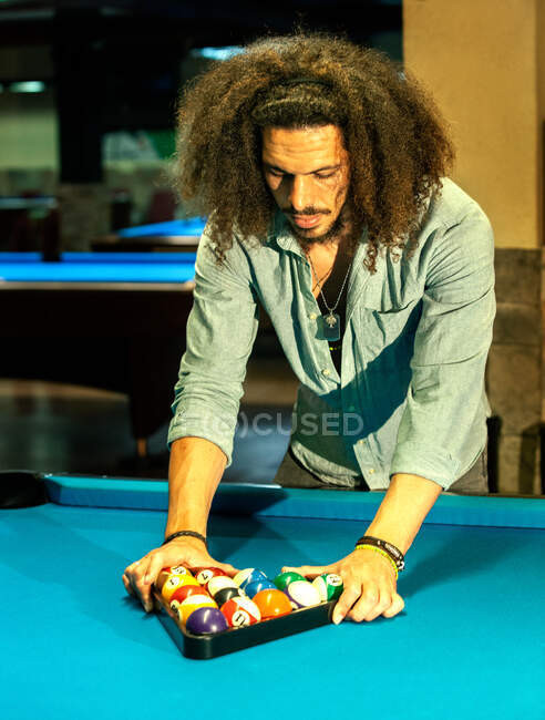 Homem étnico sério com cabelo encaracolado fazendo pirâmide de bolas para começar a jogar bilhar — Fotografia de Stock