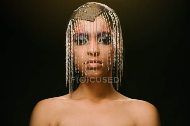 Confident ethnic female model wearing headdress with chains looking at camera on black background in studio — Stock Photo