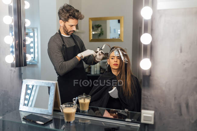 Visão lateral de fios de penteado mestre étnico focado masculino de cliente feminino antes de tingimento na técnica de balayage — Fotografia de Stock