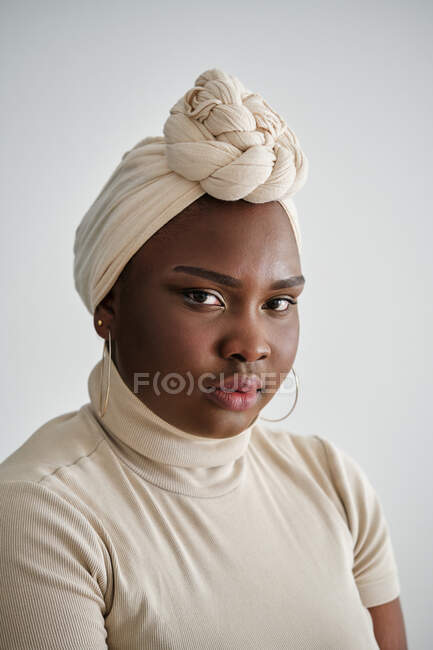 Gorgeous young African female model in stylish traditional turban standing against white background and looking at camera — Stock Photo