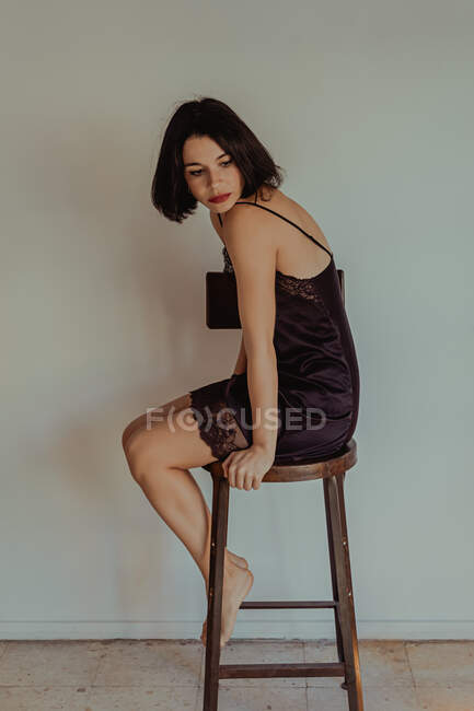 Side view of tender female in nightgown sitting on wooden stool at home — Stock Photo