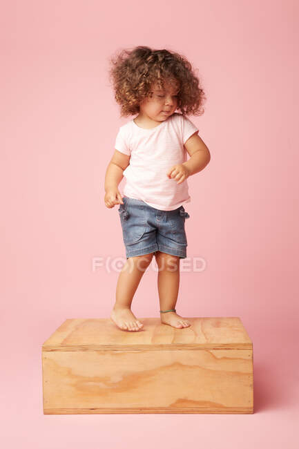 Encantador niño descalzo en camiseta y pantalones cortos de mezclilla con pelo rizado con los ojos cerrados bailando en la plataforma de madera - foto de stock