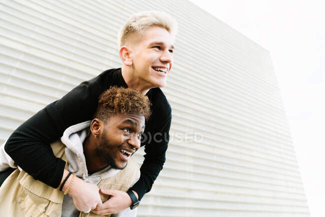 From below of cheerful young black boy giving piggyback ride to joyful friend while spending time together in city park — Stock Photo