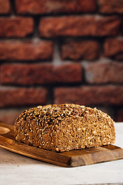 Délicieux pain complet sur planche à découper sur table — Photo de stock