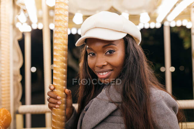 Vista laterale della femmina afro-americana su allegro andare in giro sorridendo alla fotocamera mentre intrattenere nel parco divertimenti in serata — Foto stock