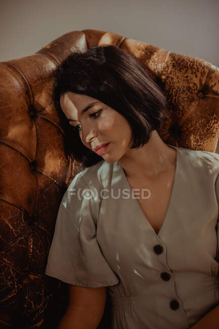 From above of peaceful female sitting in shabby leather chair while relaxing at home and looking away — Stock Photo