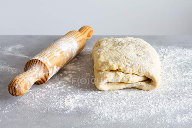 Wooden rolling pin near soft dough with flour during cooking process in countertop — Stock Photo