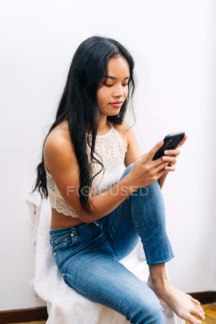 Lange Haare Asiatin sitzt zu Hause mit einem Mobiltelefon — Stockfoto