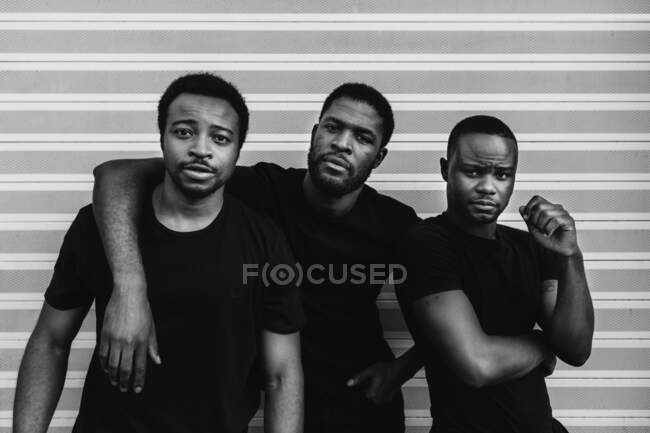 Серйозні афроамериканські друзі в чорних футболках стоять поруч, дивлячись на камеру на світлому фоні. — стокове фото