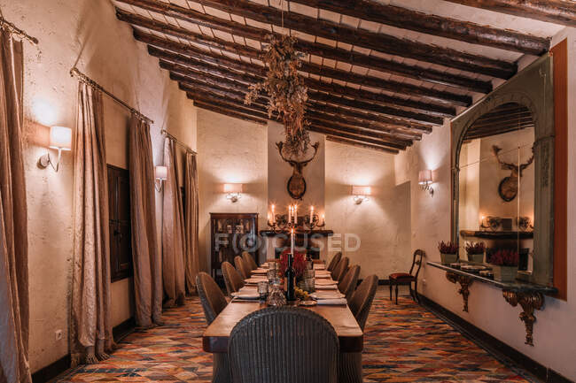 Interior da sala de jantar com mesa de madeira com talheres e pratos decorados com flores para o jantar — Fotografia de Stock
