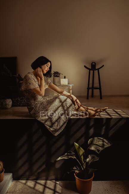 Fêmea delicada no vestido sentado no quarto com várias plantas em vaso em casa — Fotografia de Stock