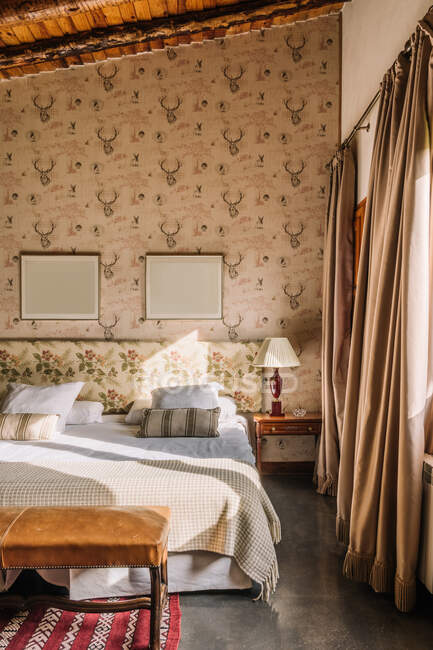 Інтер'єр стильної спальні зі зручним ліжком, покритим ковдрою біля вікна, прикрашеного шторами — стокове фото