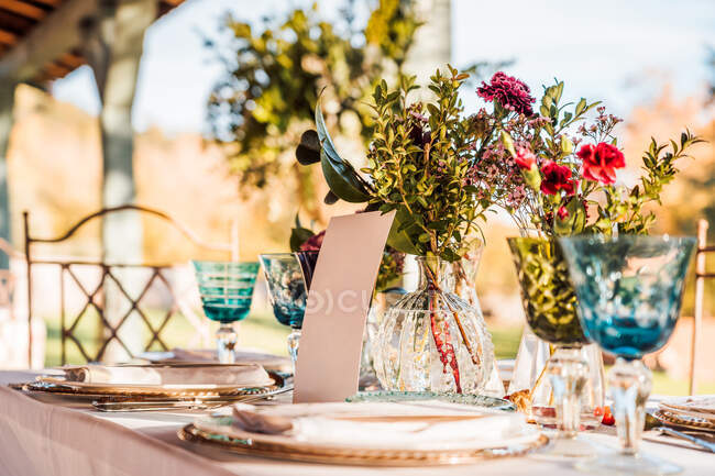 Крупним планом подається святковий стіл з кришталевими келихами столярна серветка на тарілці біля букету свіжих квітів для весілля та картки меню — стокове фото