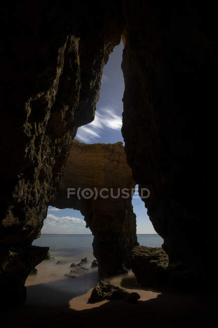 Através de paisagens rupestres vista de formações rochosas ásperas na praia de Pinhao arenosa contra o mar sob céu nublado no Algarve Portugal — Fotografia de Stock