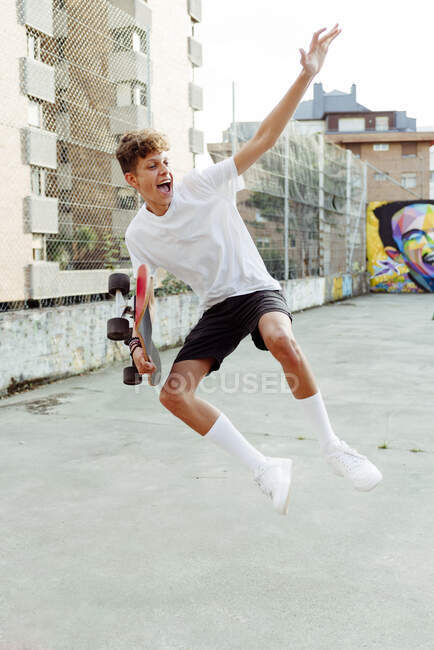 Handsome caucasian teenager with skateboard jumping and shouting in the street — Stock Photo
