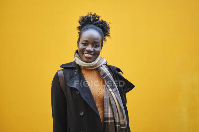 Jovem mulher étnica feliz em roupa elegante com pão de cabelo afro olhando para a câmera com sorriso de dente — Fotografia de Stock