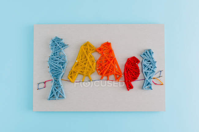 Kreatives Schnurkunstwerk in Form von Vögeln, die auf einem Ast auf Karton vor blauem Hintergrund picken — Stockfoto