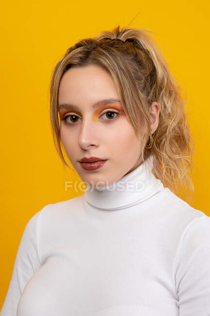 Preciosa joven hembra en ropa blanca mirando a la cámara mientras está de pie sobre fondo amarillo en el estudio - foto de stock