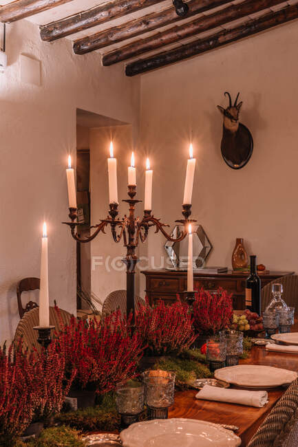 Интерьер столовой с деревянным столом со столовыми приборами и тарелками, украшенными цветами на ужин — стоковое фото