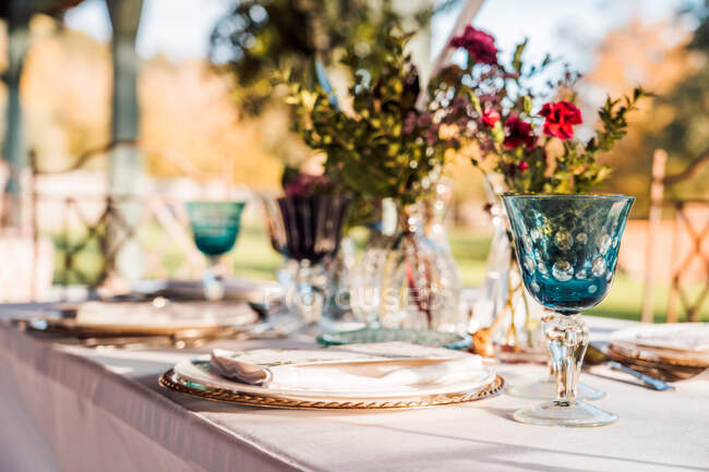 Primer plano de la mesa festiva servida con vasos de cristal cubiertos servilleta en el plato cerca de ramo de flores frescas para la boda - foto de stock