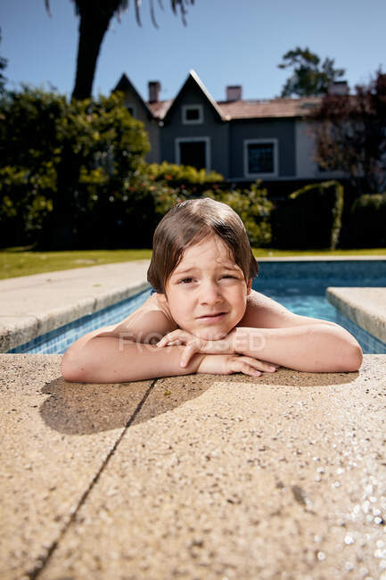 Nachdenkliches Kind lehnt am Beckenrand und ruht sich nach dem Schwimmen am sonnigen Tag aus — Stockfoto