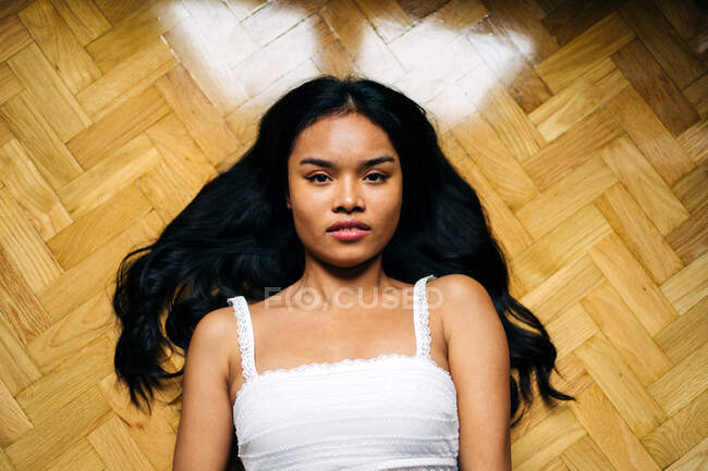 Довге волосся брюнетка азіатська жінка лежить на підлозі вдома і дивиться на камеру — стокове фото