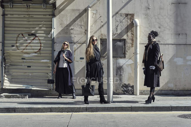 Mulheres diversas confiantes no desgaste moderno com acessórios em pé no pavimento perto da estrada da cidade — Fotografia de Stock