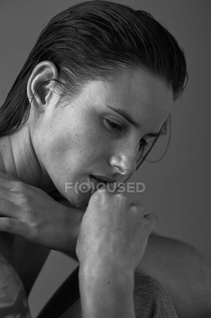 Black and white of serious female with makeup and freckles on nose gently touching skin and looking away — Stock Photo