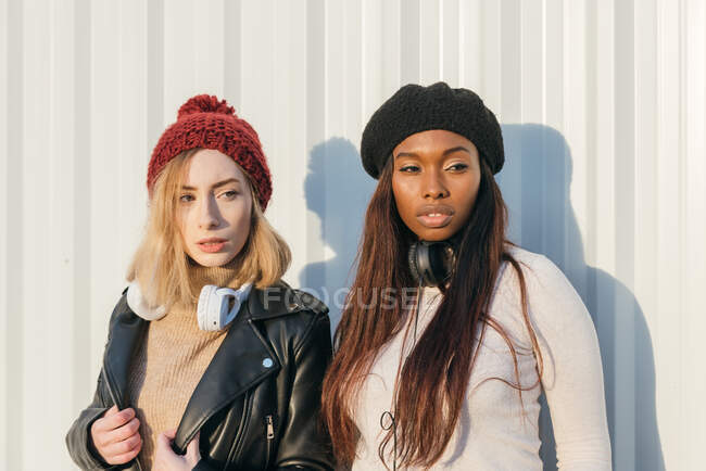 Прохолодні багаторасові жіночі моделі в модному одязі, що стоїть біля металевої стіни в місті в сонячний день — стокове фото