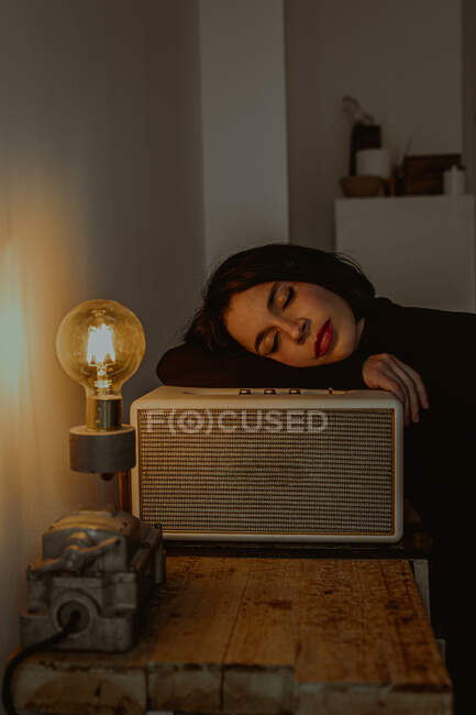 Vue latérale d'une femme rêveuse penchée sur un poste de radio dans une pièce rétro et les yeux fermés — Photo de stock