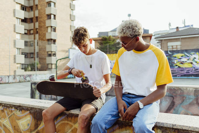Two handsome teenage boys sitting on the wall repairing a skateboard — Stock Photo