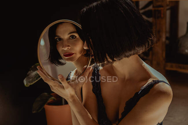 Мирная женщина, сидящая на полу в комнате и отражающаяся в круглом зеркале и смотрящая в камеру — стоковое фото