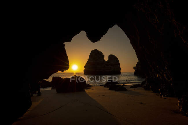 À travers la grotte rocheuse de la plage de sable pittoresque de l'océan contre le ciel couchant à Praia do Camilo en Algarve, Portugal — Photo de stock