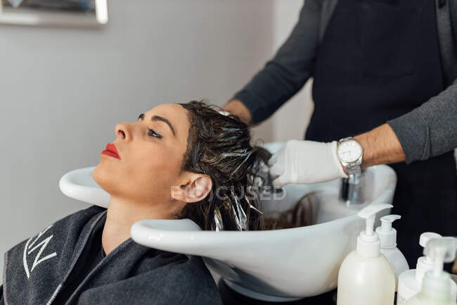 Після нарізання та фарбування у сучасному салоні краси самець перукаря миє волосся самки - клієнтки в раковині. — стокове фото