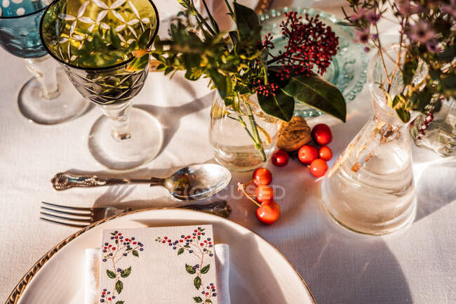 High angle of served festive table with crystal glasses cutlery napkin on plate near bunch of fresh flowers for wedding and menu card — Stock Photo