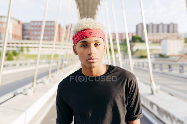 Handsome black boy with headscarf standing in the middle of the bridge looking at camera — Stock Photo