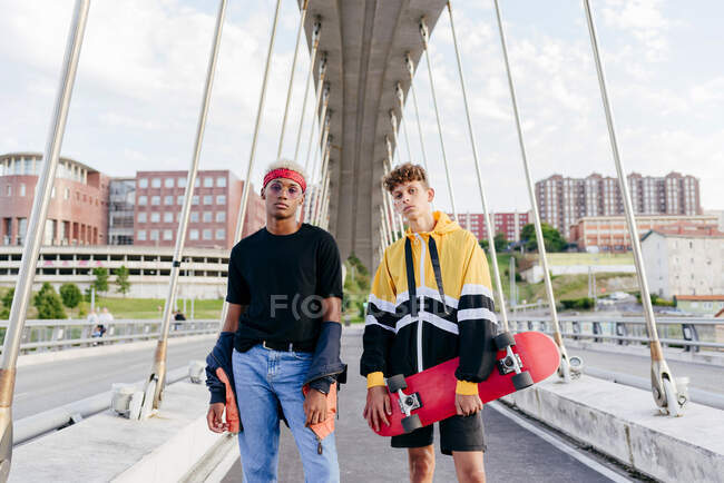 Dois adolescentes bonitos com skate em pé na ponte — Fotografia de Stock