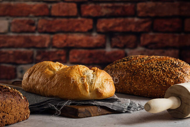 Білий та житній хліб з крупами та апетитною скоринкою на обробній дошці проти цегляної стіни у випічці — стокове фото