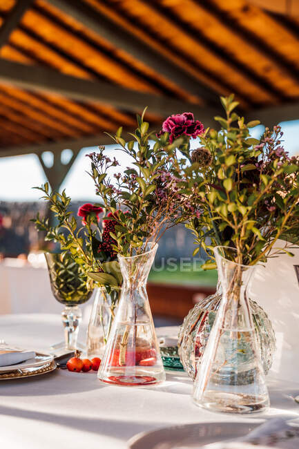Close-up de vasos de vidro transparentes com cachos de flores frescas colocadas na mesa para o evento — Fotografia de Stock