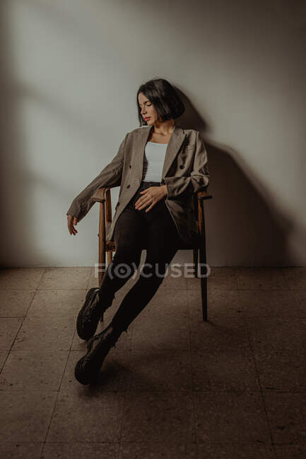 Mulher relaxada vestindo roupas da moda sentada na cadeira enquanto toca o cabelo com os olhos fechados — Fotografia de Stock