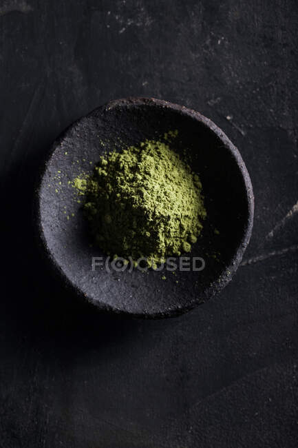 Vista superior de las hojas de té verde en polvo en tazón de piedra colocado en la mesa negra para el té y el sabor - foto de stock
