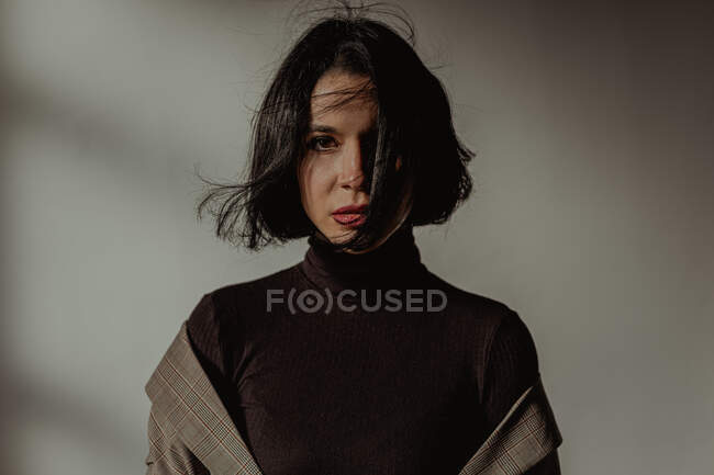 Tranquil female with flying hair and in black turtleneck looking at camera in room against white wall — Stock Photo
