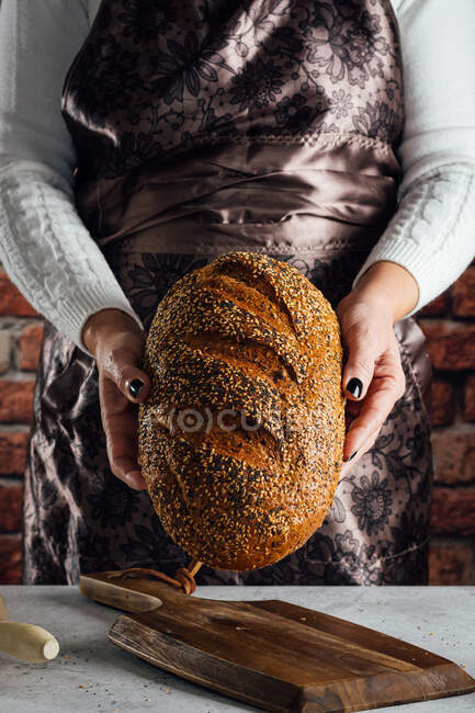 Crop anonymous female baker holding bread with sunflower seeds on table in bakehouse — Stock Photo