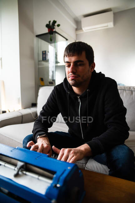 Hombre ciego serio sentado en el sofá y escribiendo en la máquina de escribir con el código del sistema táctil - foto de stock