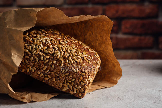 Pão inteiro saboroso com crosta marrom e sementes de girassol em cima na mesa à luz do dia — Fotografia de Stock