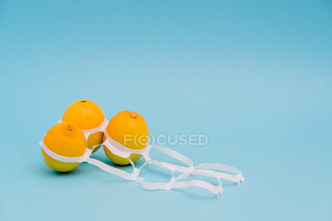 Helle ganze reife und saftige Zitronen zwischen dünnen Plastikverpackungsringen mit Löchern — Stockfoto
