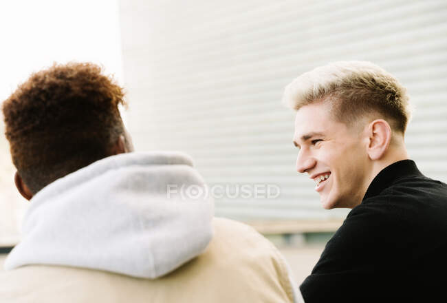Back view of happy young multiracial male friends in trendy outfits standing on city street near modern building — Stock Photo