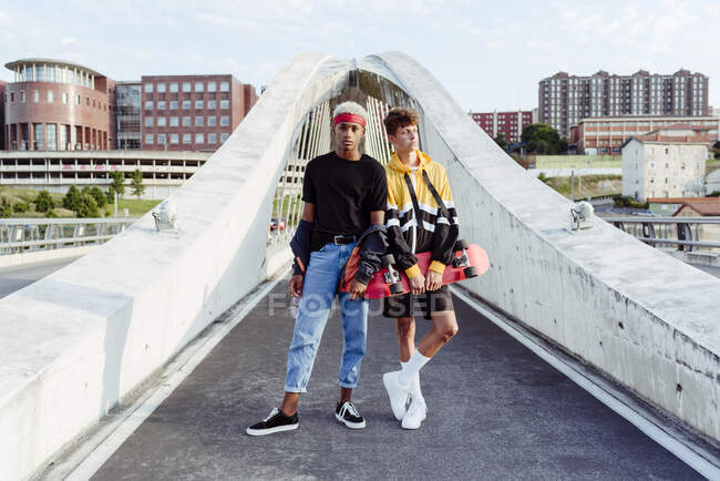 Dos guapos adolescentes con monopatín de pie en el puente - foto de stock