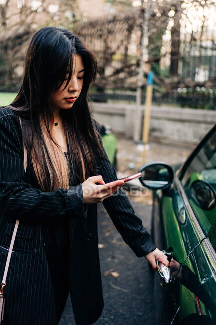 Capelli lunghi bruna donna asiatica che apre un'auto con il telefono cellulare — Foto stock