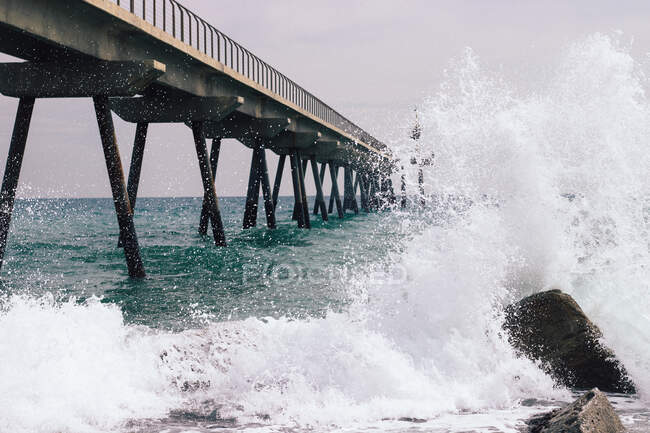 Scenery view of foamy ocean with splattering water flow and stones under pier in daytime — Stock Photo